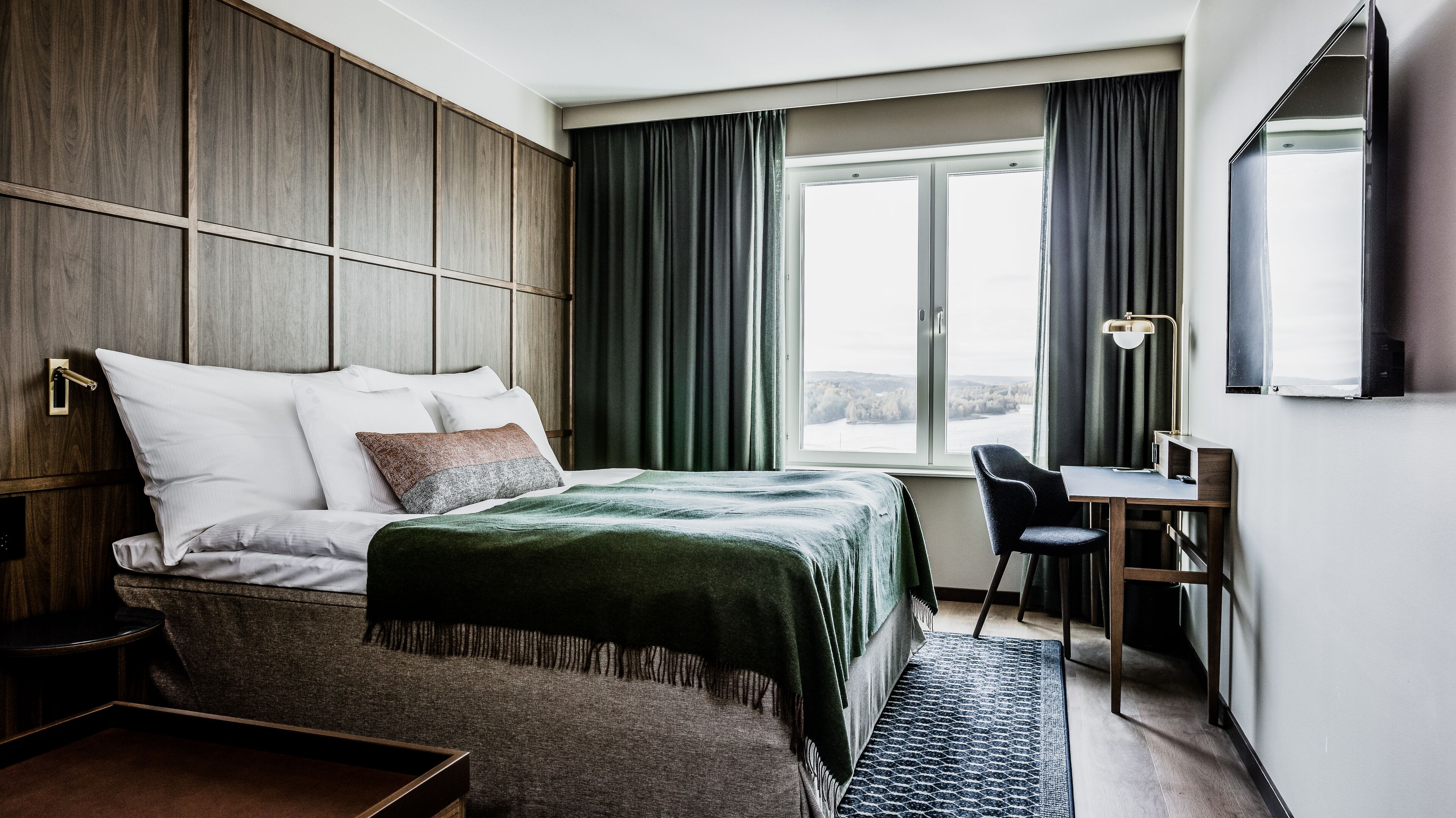 A modern hotel room with a large bed, a desk, and a view of a body of water.
