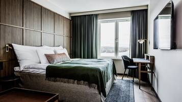 A modern hotel room with a large bed, a desk, and a view of a body of water.
