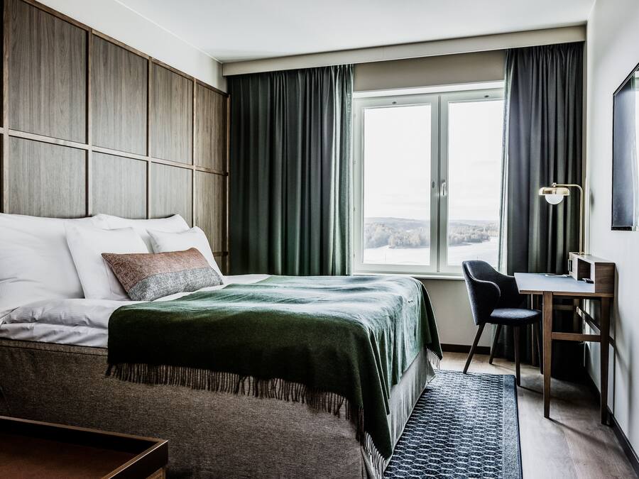 A modern hotel room with a large bed, a desk, and a view of a body of water.