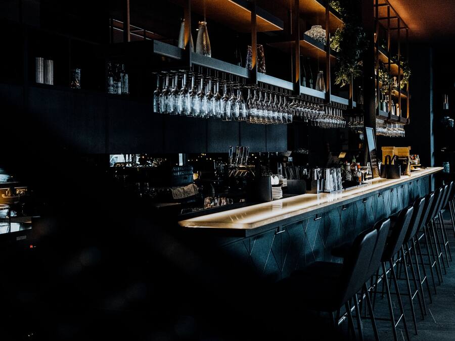 A bar area with a long counter, multiple shelves with glasses, and a modern design.