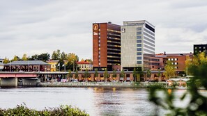A hotel with a clock tower, a river in the foreground, and various buildings in the background. - Clarion Hotel Umea (Umea)