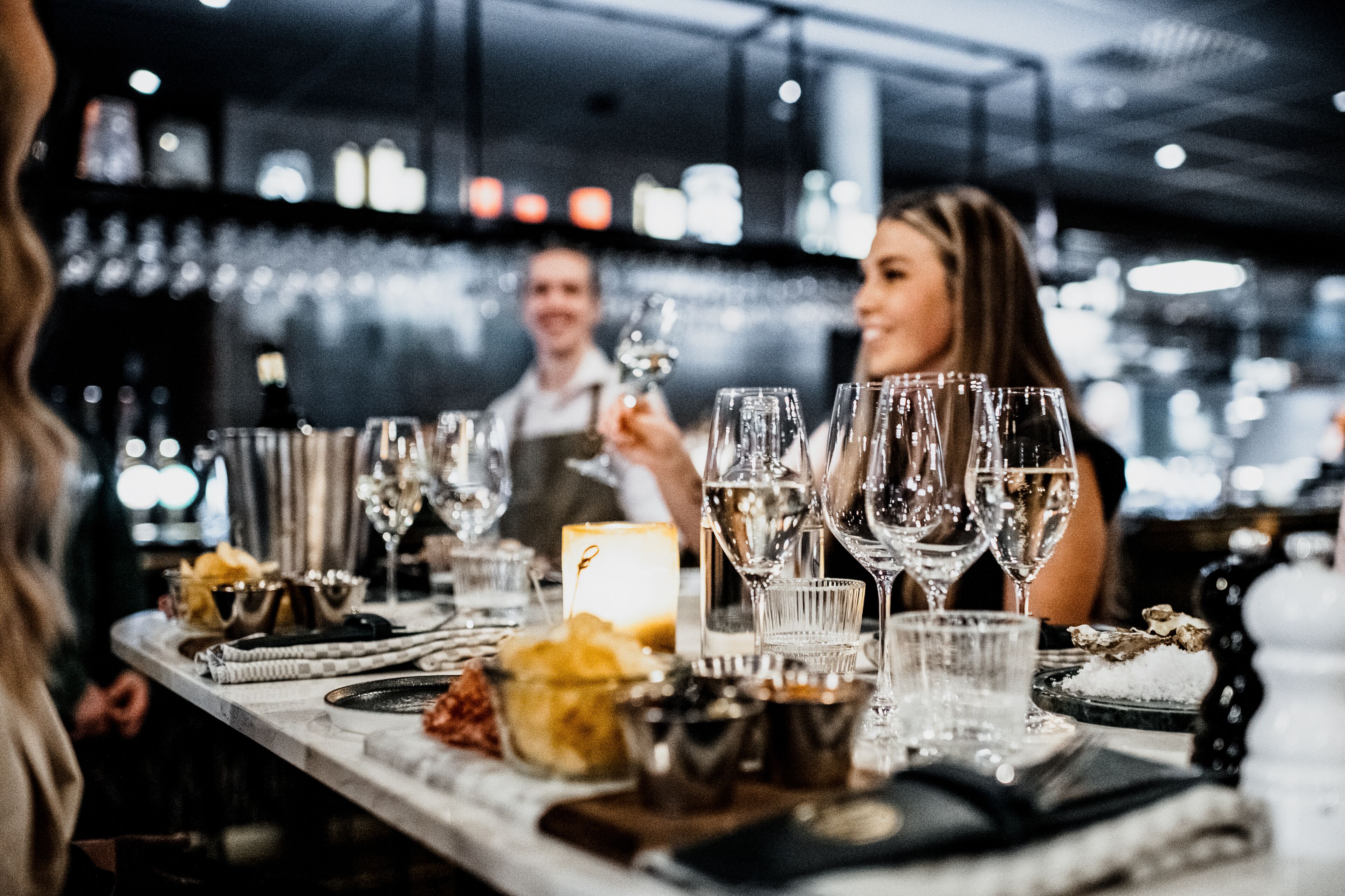 A bar setting with multiple glasses and bottles, a candle, and a bowl of snacks.