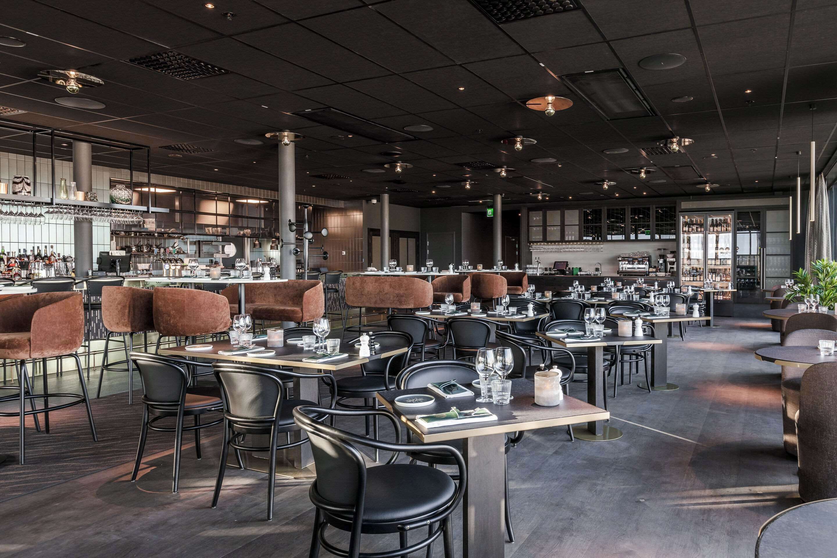 A spacious restaurant with multiple dining tables and chairs, a bar area, and a modern interior design.