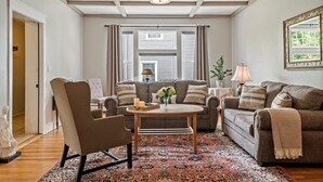 A living room with a sofa, armchair, and coffee table, a patterned rug, and a ceiling light fixture.
