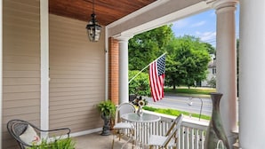A porch with a table and chairs, an American flag, and a view of a street.