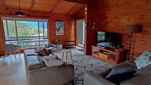 A cozy living room with a large TV, wooden walls, and a view of the outdoors. - ALPINE ALLURE - ALL SEASONS WONDER (Tawonga South)