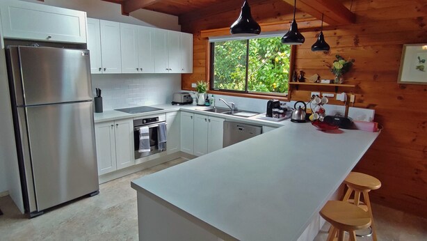 A modern kitchen with white cabinets, stainless steel appliances, a large island, and wooden accents. - ALPINE ALLURE - ALL SEASONS WONDER (Tawonga South)