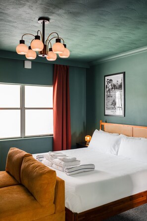 Ein Schlafzimmer mit einem Bett, einem hölzernen Kopfteil, einem Nachttisch mit Lampe, einem gerahmten Foto an der Wand und einem Fenster mit Vorhängen.