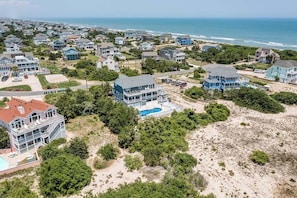 A coastal residential area with multiple houses, a swimming pool, and a beach in the background. - Mermaid Manor | 435 ft to the beach | Private Pool, Hot Tub (Corolla)