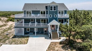 Ein zweistöckiges Strandhaus mit Balkon, überdachter Veranda und kleinem Garten.