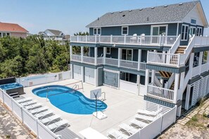 Una casa de dos pisos con piscina, varios balcones y un área exterior techada con sillones de descanso.