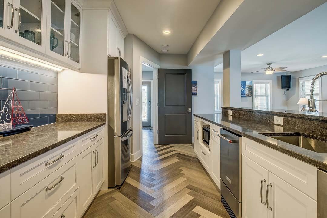 A modern kitchen with white cabinetry, stainless steel appliances, and a herringbone wood floor.