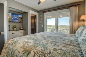 Un dormitorio con una cama grande, un televisor montado en la pared, una ventana con cortinas y vistas al exterior.