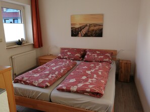Ein Doppelbett mit floralem Bettbezug, ein hölzerner Kopfseitenverkleidung, ein Nachttisch, ein Fenster mit Blick auf Gebäude und ein Gemälde an der Wand.