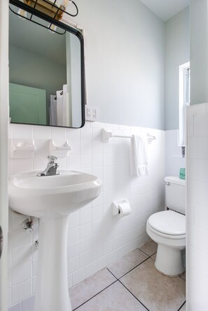 Et badeværelse med hvid vask, spejl, toilet og håndklædestang.