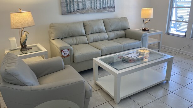 A modern living room with a beige sofa, a glass coffee table, and a painting of birds on a fence. - Villa in Rotonda West with huge screened lanai and canal view (Rotonda West)