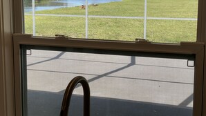 A view through a window with a metal grill, overlooking a grassy area with a body of water and a distant building. - Villa in Rotonda West with huge screened lanai and canal view (Rotonda West)