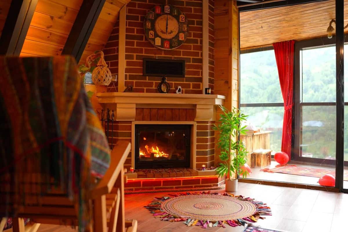 A cozy room with a fireplace, a clock, and a large window with curtains.