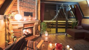 A cozy loft bedroom with a fireplace, a comfortable seating area, and a view of the outdoors. - Puleri Dağ Evi (Camlihemsin)