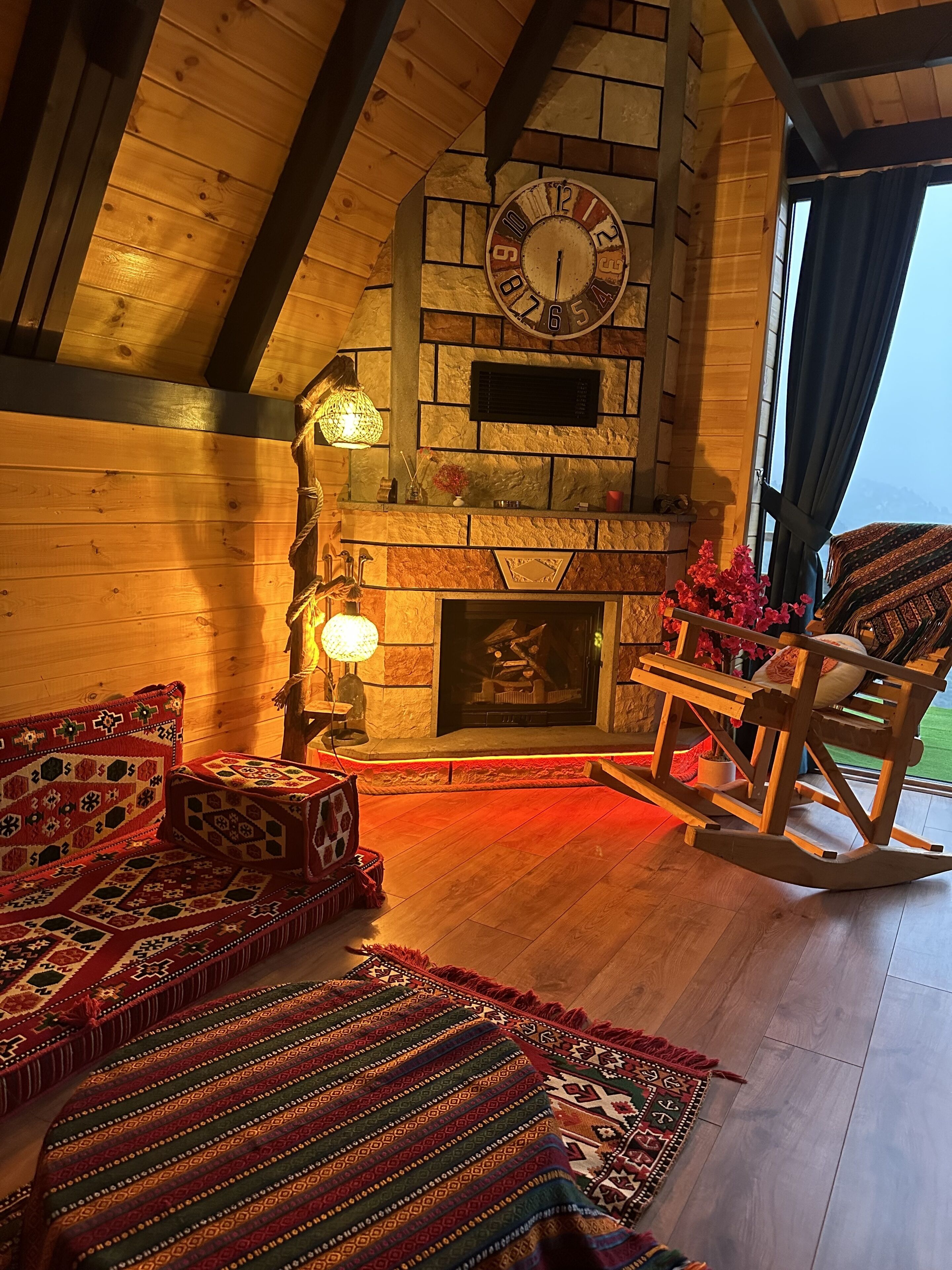 A cozy log cabin interior with a stone fireplace, wooden beams, and traditional rugs.