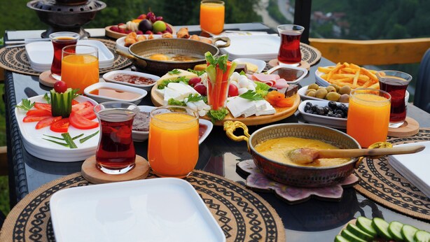 A table set with a variety of dishes and drinks, overlooking a mountainous landscape. - Puleri Dağ Evi (Camlihemsin)