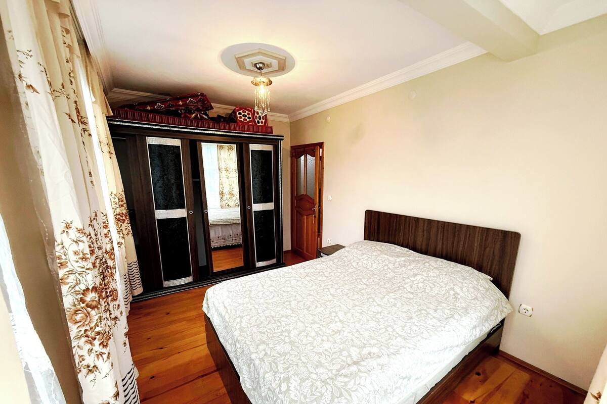A bedroom with a bed, wooden floor, a wardrobe, and a ceiling light fixture.