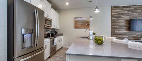 A modern kitchen with stainless steel appliances, a central island, and a wooden accent wall.