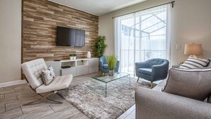 Un salon moderne avec un téléviseur à écran plat fixé à un mur en bois, une table basse en verre et deux canapés.