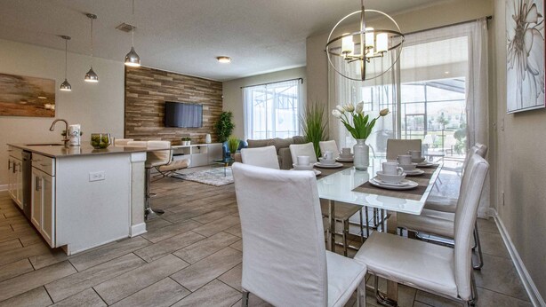Une cuisine moderne dotée d’un îlot central, un coin repas avec une table en verre et des chaises blanches, et un espace de détente avec un canapé et un téléviseur.