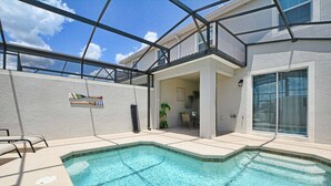 Une piscine entourée de parois en verre, un patio couvert et une vue sur le jardin arrière.