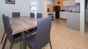 Een eethoek met een houten tafel en stoelen, een keuken met witte kasten, en een klein keukeneiland met een spoelbak.