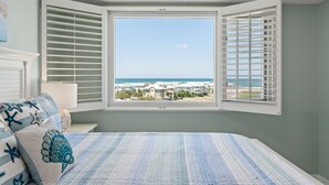 Une chambre avec une grande fenêtre, un lit avec une literie à rayures et une vue sur une plage et des bâtiments.