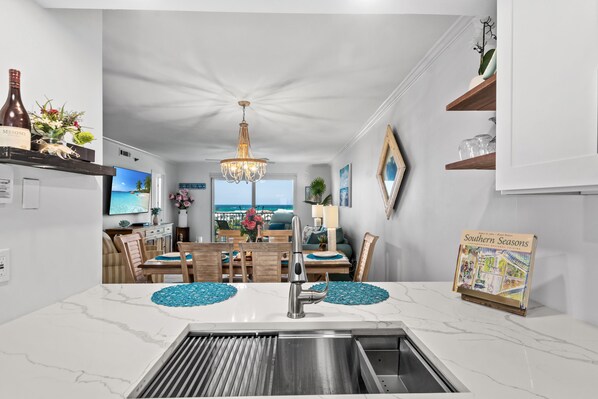 A modern kitchen with a central island, a chandelier, and a view of the ocean through large windows. - 716 Stunning Gulf Views • Pools • Hot Tubs • Sleeps 6 • Book Oct 22nd (Destin)