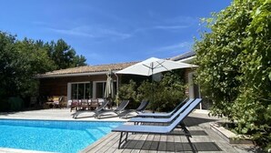 Una terraza de madera con piscina, sillas de descanso y un espacio de estar cubierto.