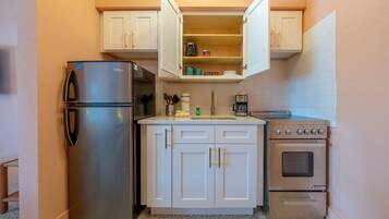A compact kitchenette with a stainless steel refrigerator, a built-in oven, and a coffee maker.