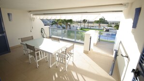 A balcony with a white table and chairs, a view of a beach, and a glass railing. - 40 - Apartamento Sugar (Tarifa)