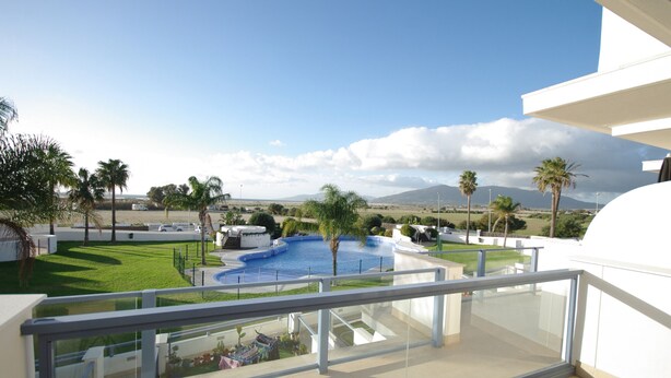 A modern hotel balcony with a clear view of a swimming pool, palm trees, and distant mountains. - 40 - Apartamento Sugar (Tarifa)