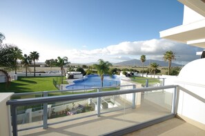 Varanda de hotel moderna com vista clara para uma piscina, palmeiras e montanhas ao longe.