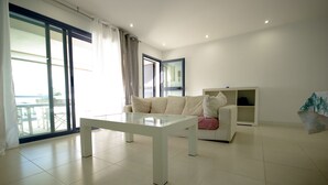 A modern living room with a glass-top table, a white sofa, and a built-in shelving unit. - 40 - Apartamento Sugar (Tarifa)