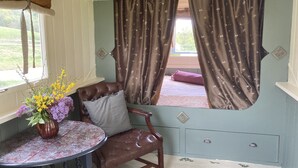 A cozy room with a window, a chair, a table with a vase of flowers, and a bed with curtains.