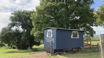 A small, single-story building with a dark blue exterior and a white-framed window. The building is labeled "H.R. ANDREWS Steam Puddling and Moulding Works." It is situated in a rural setting with a large tree in the background and a grassy area in the foreground.