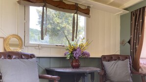 A cozy room with two brown leather chairs, a small round table with a vase of flowers, and a window with curtains.