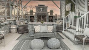 An outdoor patio with wicker furniture, a stone fireplace, and a view of a house.