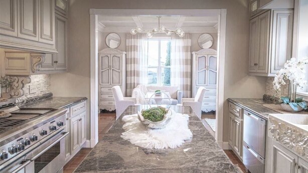 A spacious kitchen with marble countertops, a built-in stove, and white cabinetry.