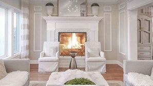 A living room with a fireplace, two white armchairs, a coffee table, and a cabinet.