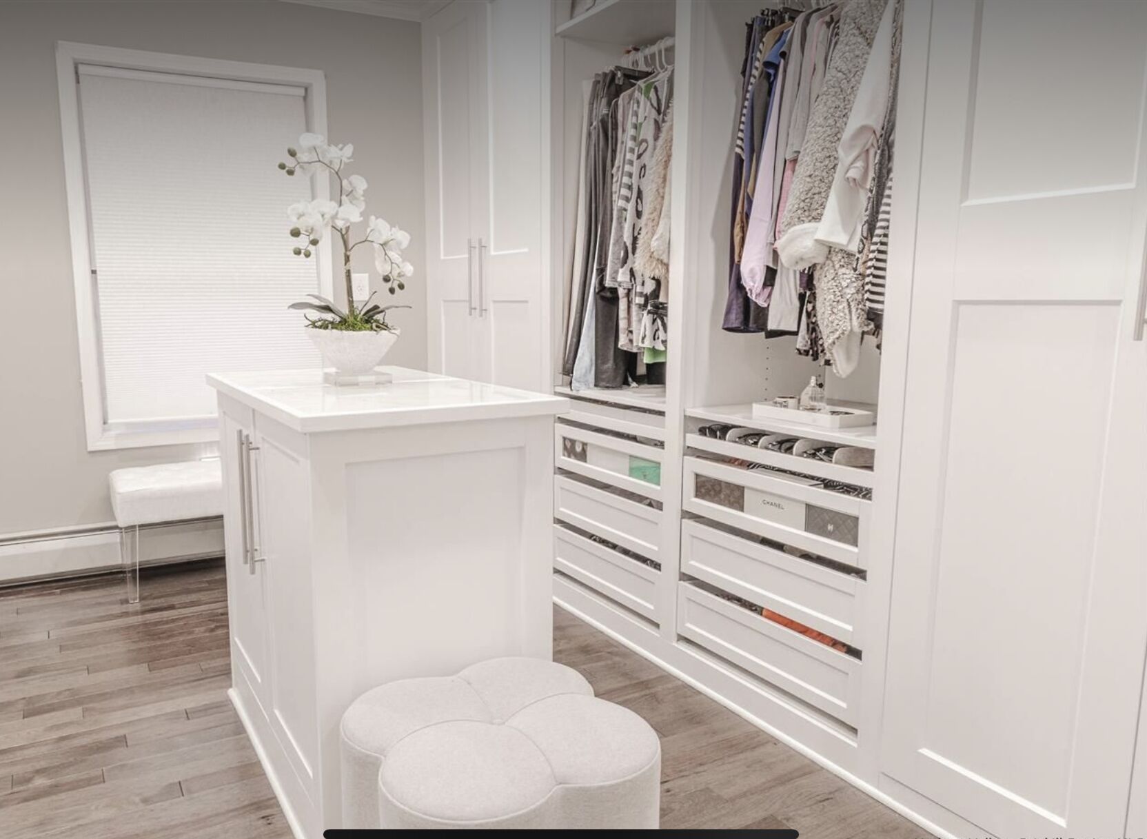 Et hvidt walk-in closet med ophængt tøj, skohold og en bænk.