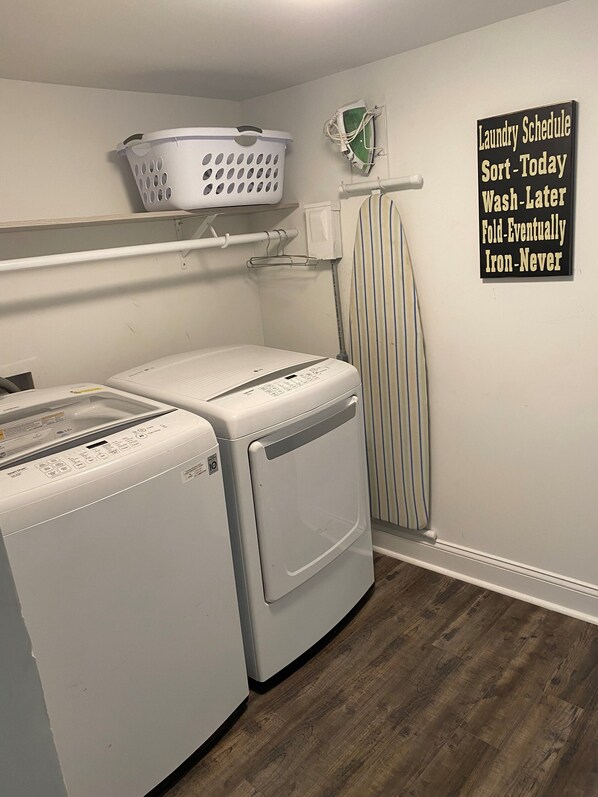 A laundry room with two front-loading washing machines, a drying rack, and a laundry schedule sign.