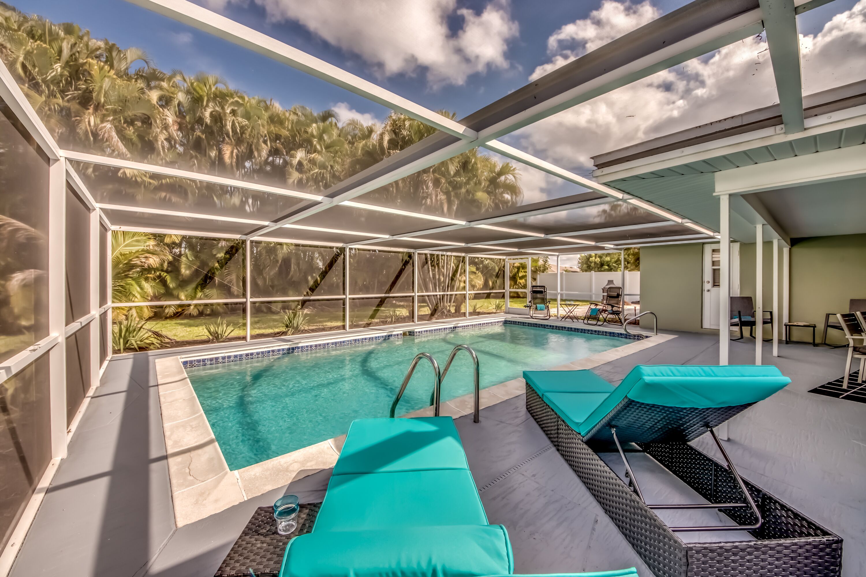 An indoor pool area with clear glass walls, two lounge chairs, and a pool with a tiled edge.