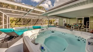 A hot tub with a glass enclosure, outdoor seating, and a view of a pool and palm trees. - Pool - Hot Tub - BBQ - Private Backyard (Cape Coral)