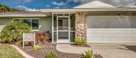 A single-story house with a garage, a stone wall, and a sign for VacationHit Property Management.